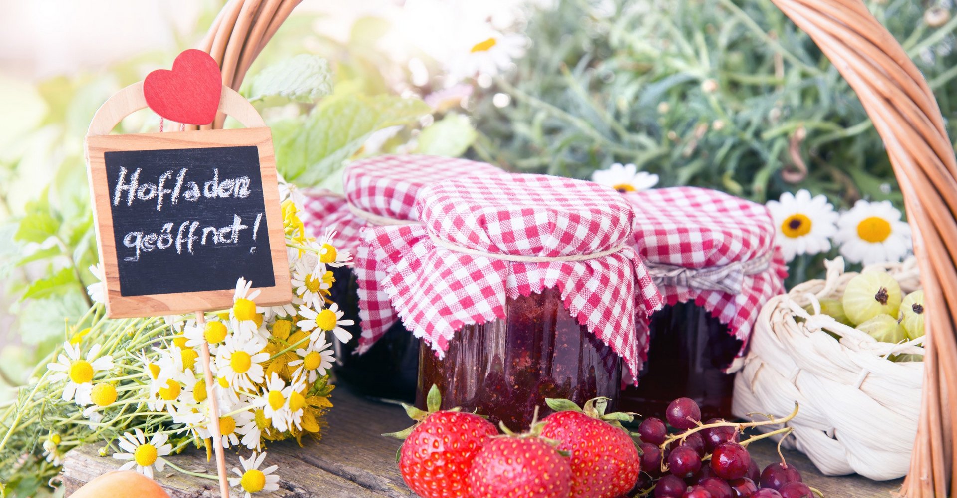 Gefüllte Marmeladengläser und Früchte auf einem Tisch mit dem Schild "Hofladen geöffnet".