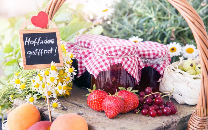 Gefüllte Marmeladengläser und Früchte auf einem Tisch mit dem Schild "Hofladen geöffnet".