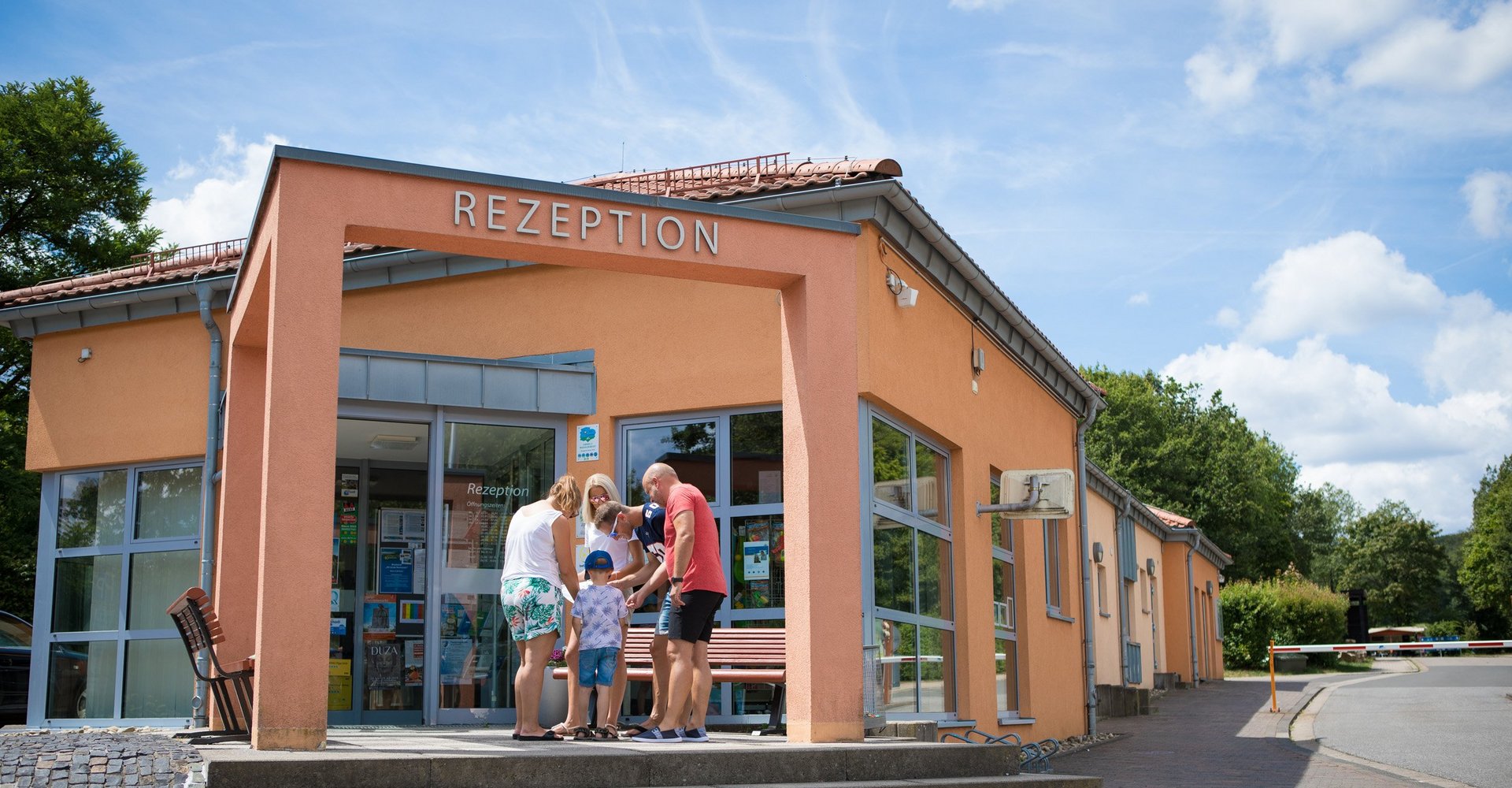 Mehrere Personen stehen vor dem orangefarbenen Gebäude des Campingplatzes und schauen auf eine Karte.