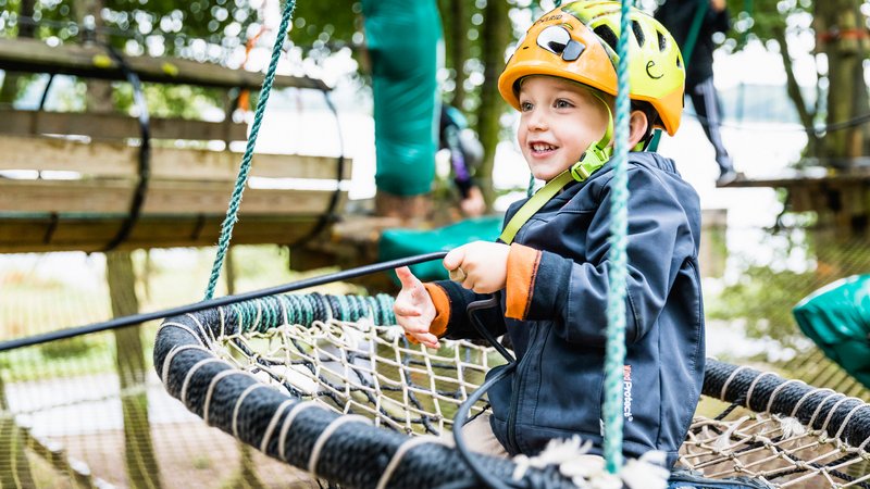 Ein Junge mit gelbem Helm zieht sich an einem Seil durch den Kletterpark.