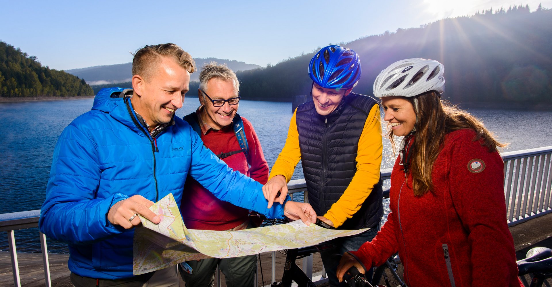 Zwei Männer in warmer Freizeitkleidung und eine Frau und ein Mann mit Fahrradhelmen auf dem Kopf beugen sich über eine Karte.