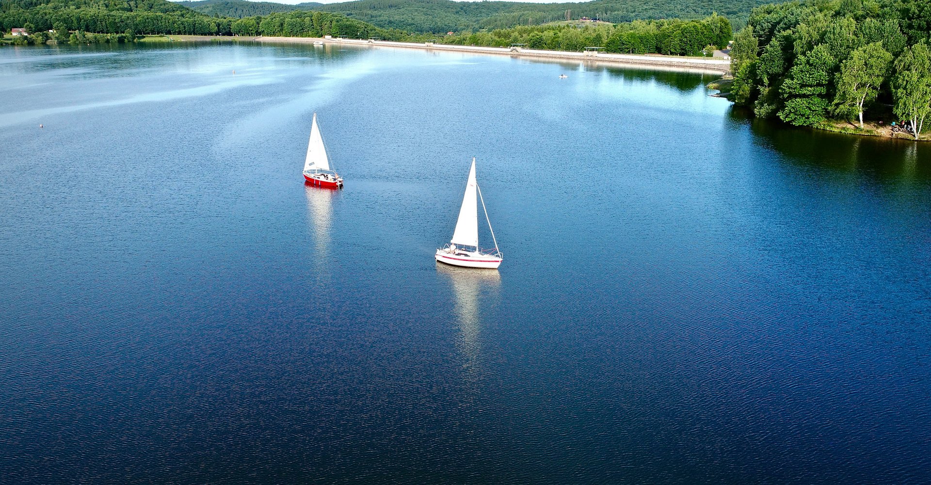 2 Segelboote segeln entlang des Staudamms.