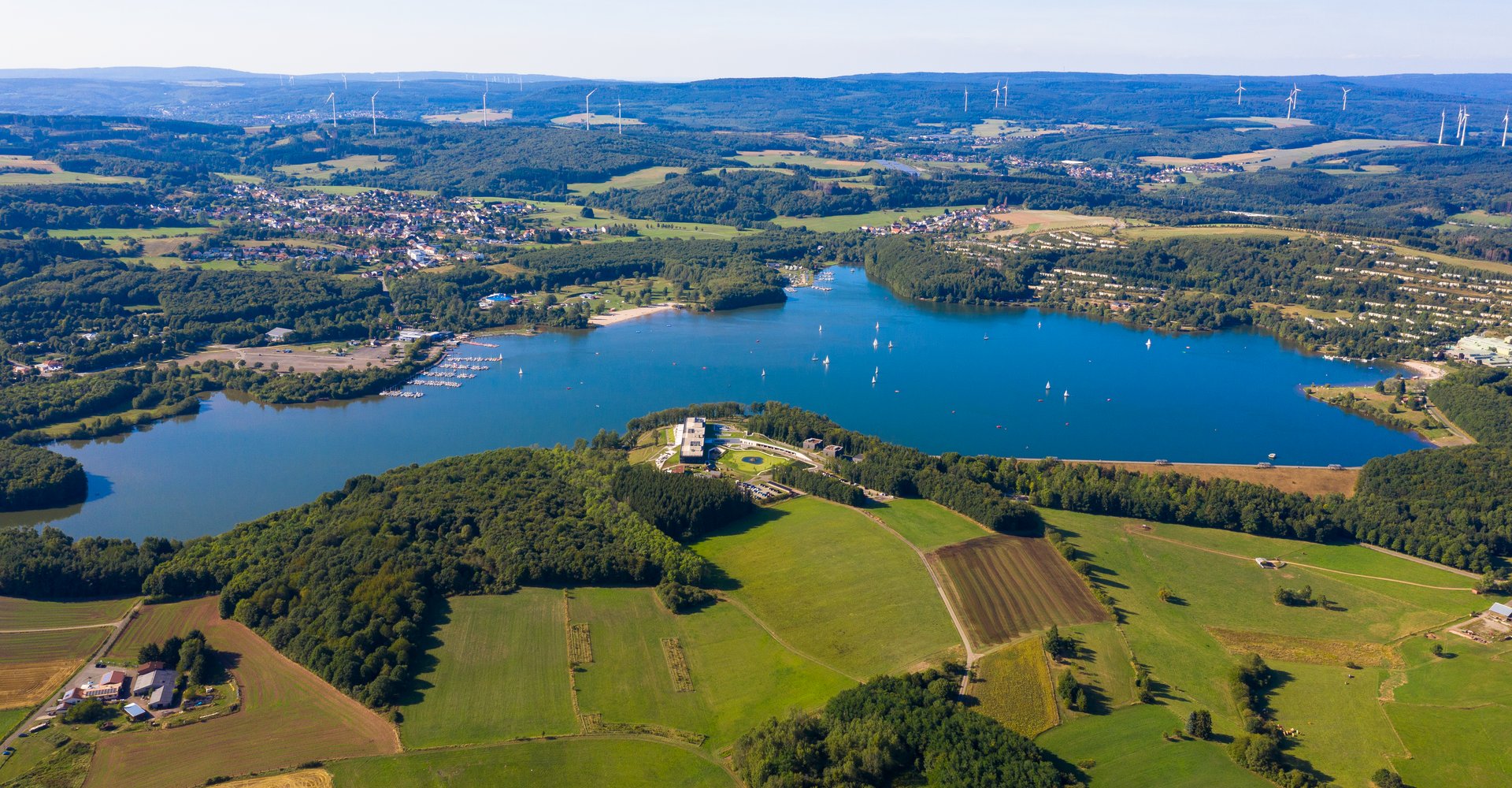 Der Bostalsee von oben. Er ist umgeben von zwei Dörfern, ganz vielen Feldern und Wald.