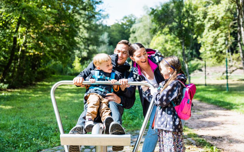 Eine Familie mit zwei Kindern nutzt eines der Spielgeräte an der Nahequelle und hat Spaß dabei.