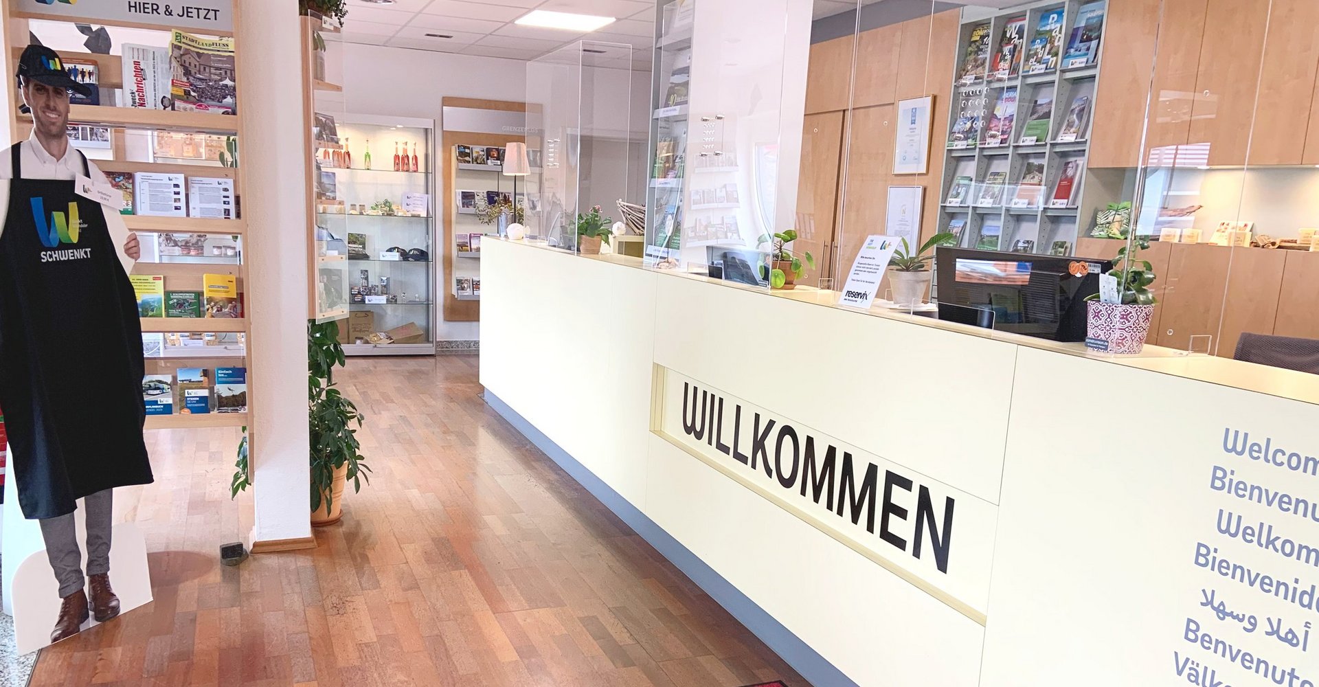 Der Eingangsbereich der Tourist-Information begrüßt die Gäste mit einem Willkommen an der langen Theke. Rundherum befinden sich Informationsbroschüren und Verkaufsartikel