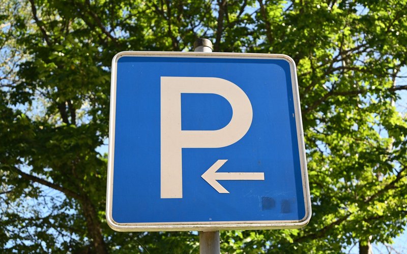 Ein blaues Parkplatzschild mit einem weißen P und einem weißen Pfeil nach links