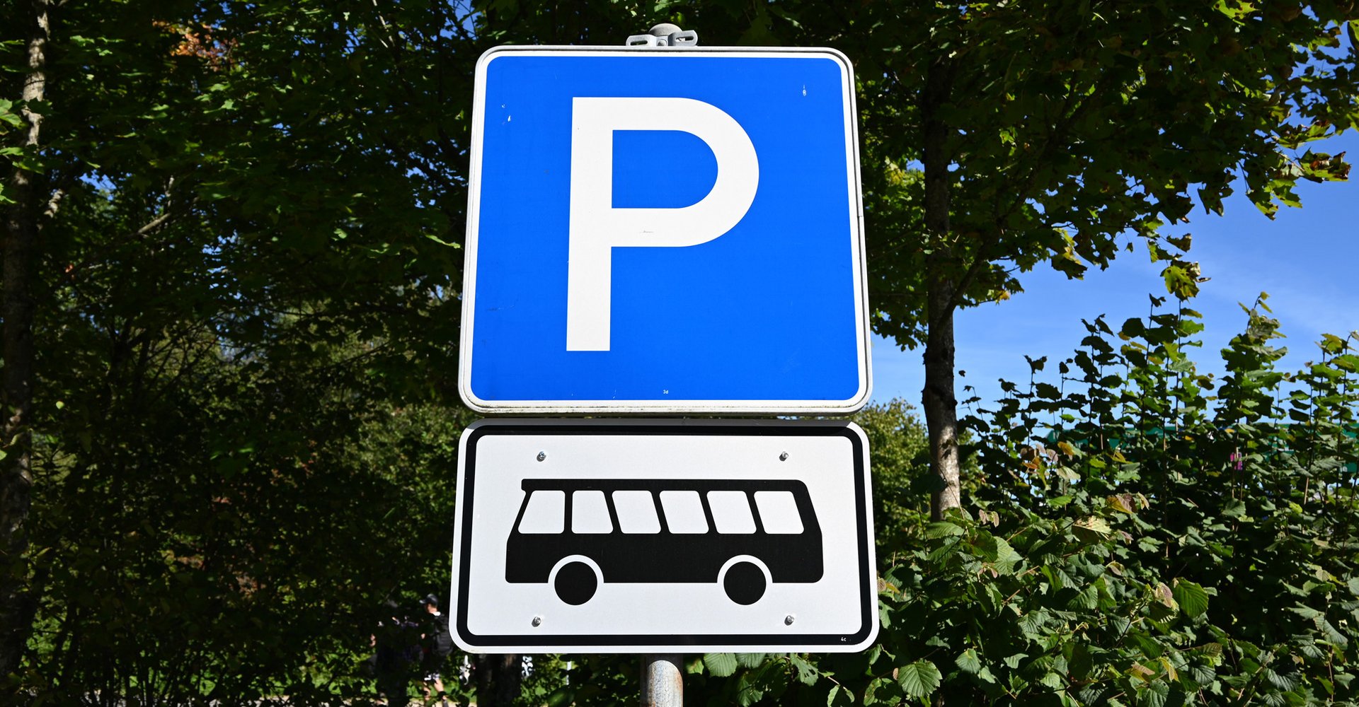 Ein blaues Parkplatzschild mit einem weißen P darin und einem Bus-Symbol darunter.