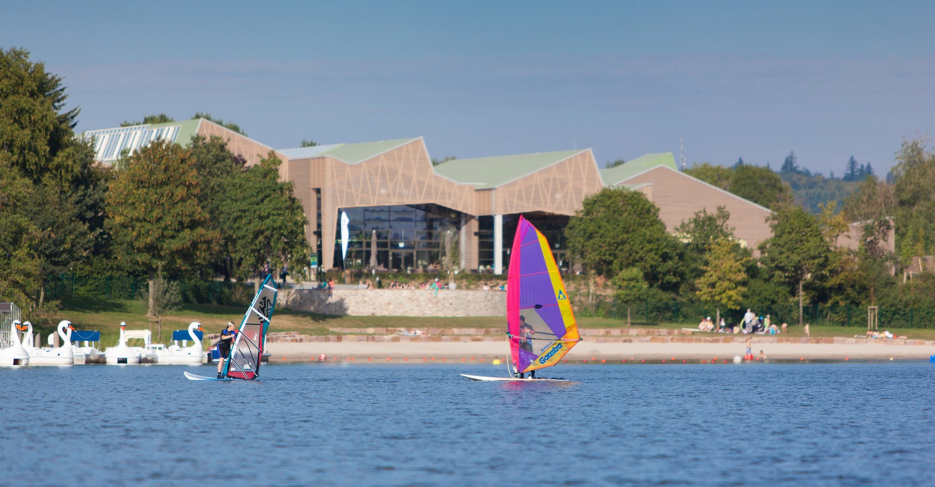 Ein Windsurfer surft vor dem Market Dome Gebäude des Center Parcs über das Wasser.