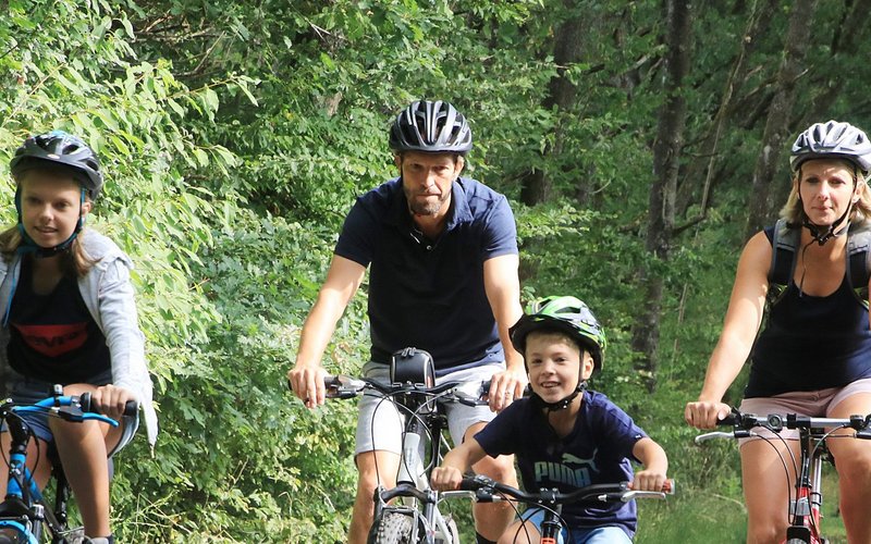 Eine Familie mit zwei Kindern fährt mit ihren Rädern auf dem asphaltierten Wendelinus-Radweg. Umgeben sind sie von Bäumen.