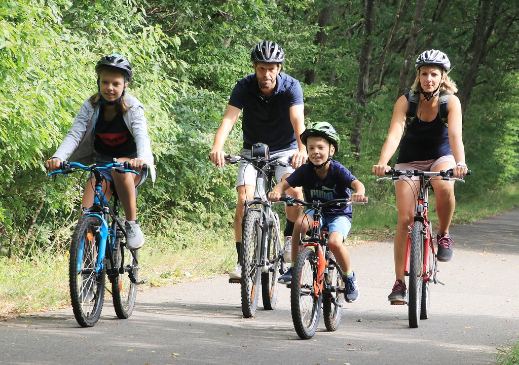 Eine Familie mit zwei Kindern fährt mit ihren Rädern auf dem asphaltierten Wendelinus-Radweg. Umgeben sind sie von Bäumen.