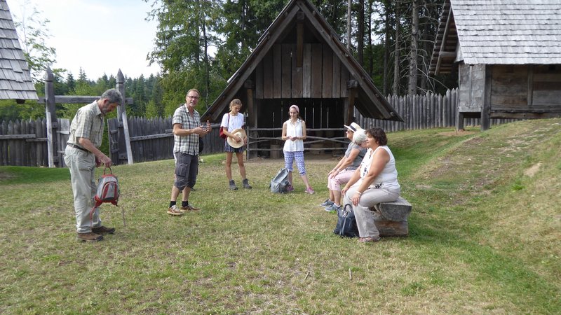 Eine kleine Gruppe von Touristen befindet sich in einem Freichlichtmuseum und nimmt an einer Führung mit einem Gästeführer teil.