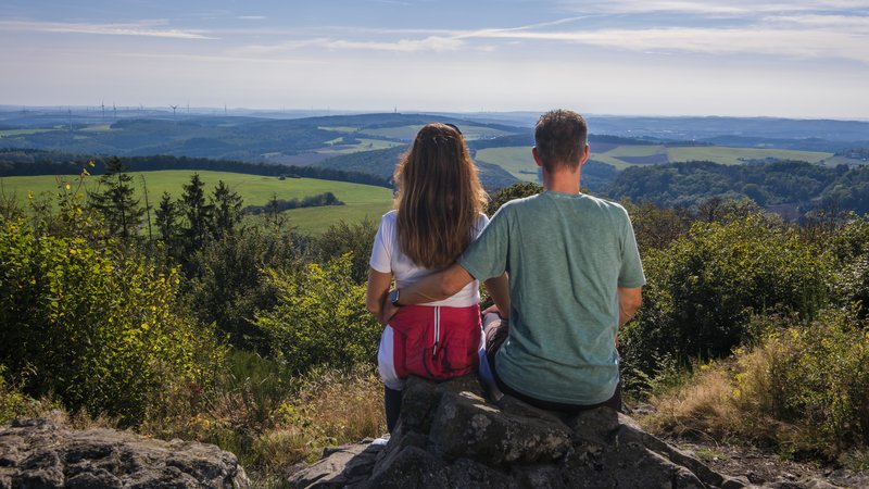Ein Mann und eine Frau sitzen auf einem Stein auf einem Berg und genießen die Aussicht.