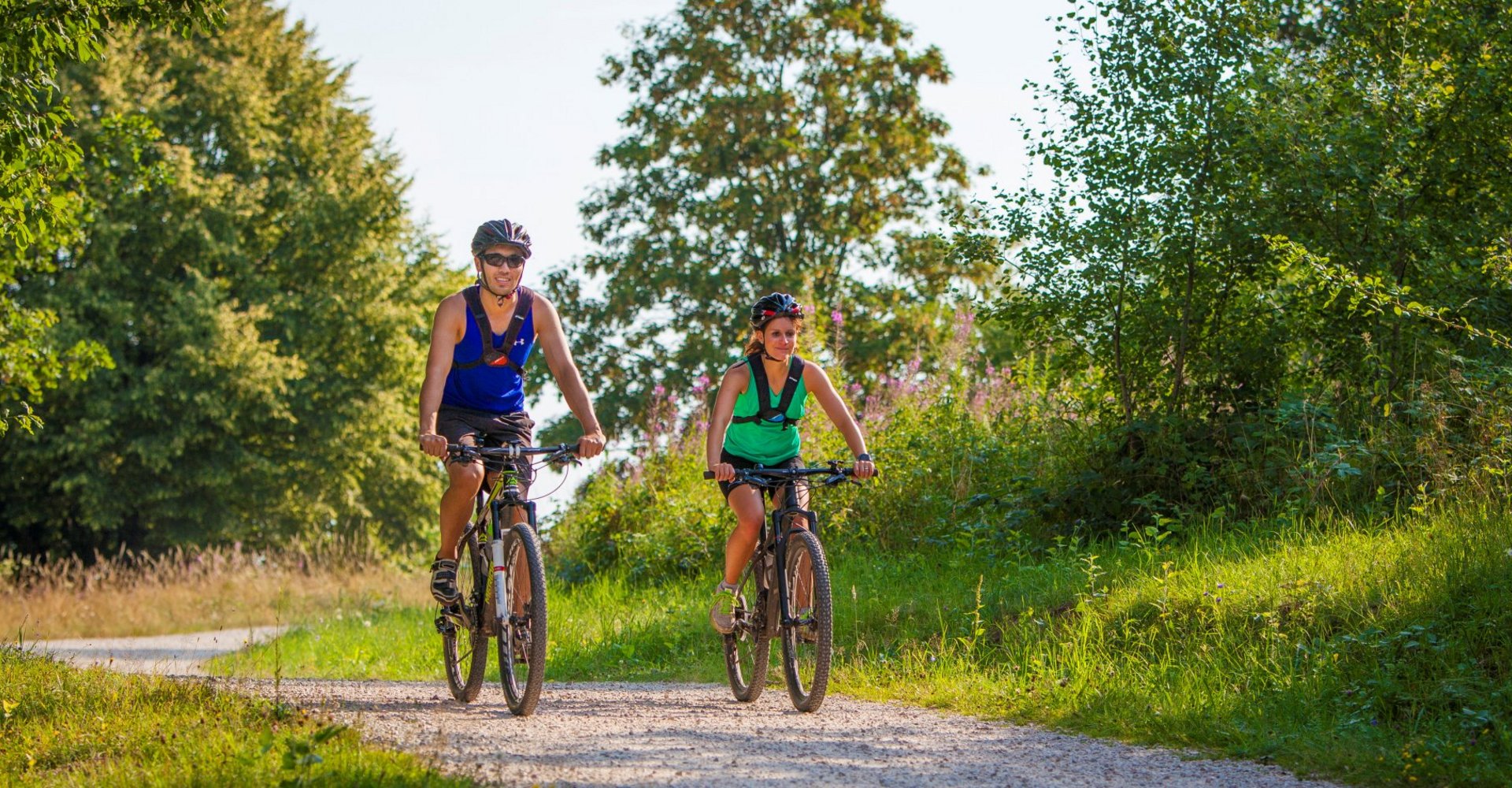 Ein Mann und eine Frau fahren mit ihren Rädern auf einem natürlichen Fahrradweg. Umgeben sind sie von üppiger grüner Vegetation