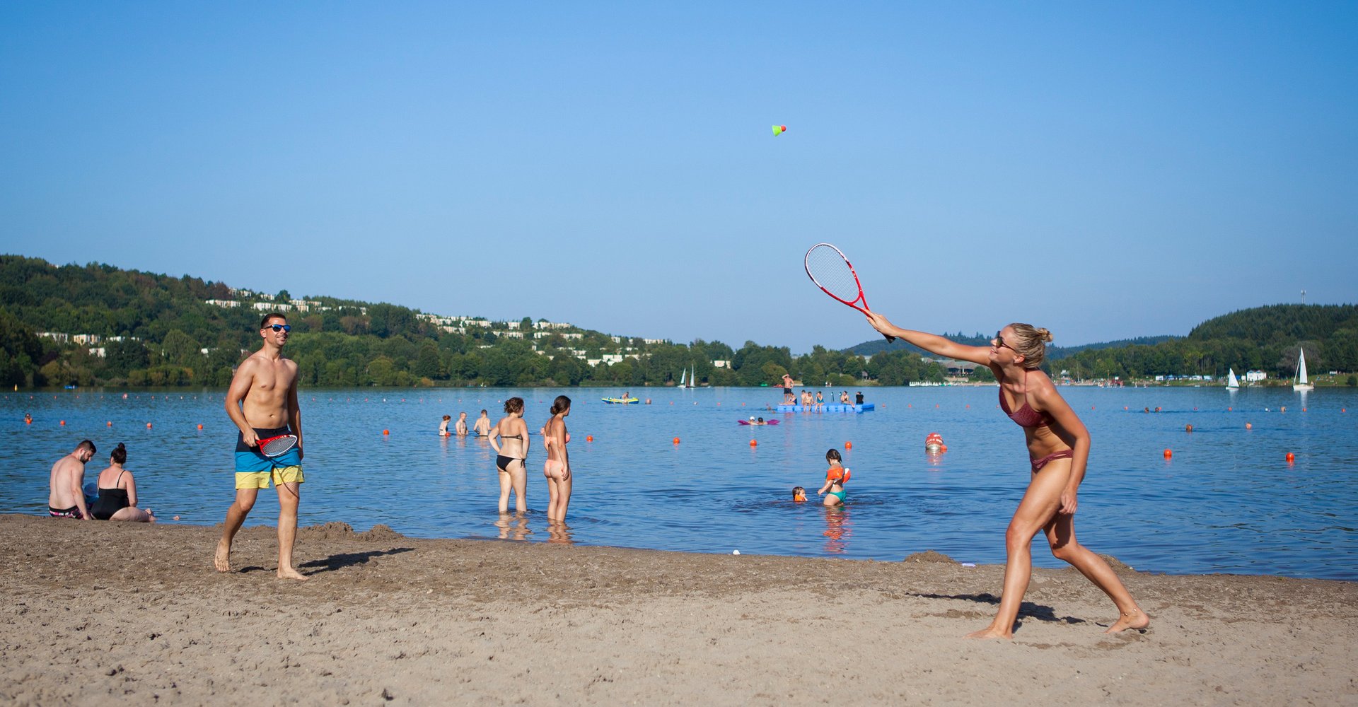 Ein Pärchen spielt am Strand Federball, während sich andere Gäste im Wasser vergnügen.
