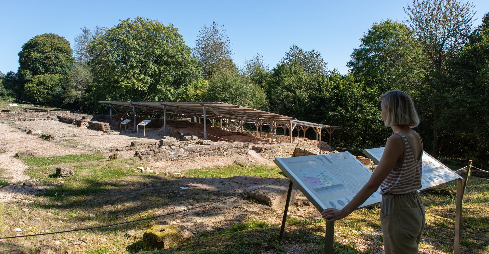 Eine Frau steht an einer Übersichtstafel und schaut auf die römischen Ausgrabungen im Vicus Wareswald.