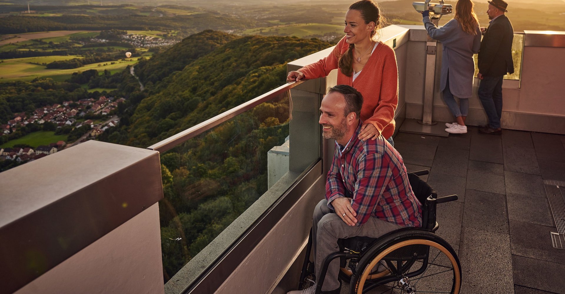 Mehrere Personen, darunter auch ein Rollstuhlfahrer, befinden sich auf der Aussichtsplattform des Schaumbergturms und genießen den Ausblick über das Sankt Wendeler Land.