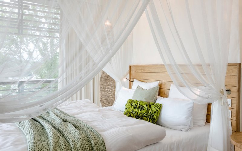 Ein gemütlich beleuchtetes Zimmer mit einem großen Himmelbett mit einer grünen Tagesdecke und vielen Kissen darauf.