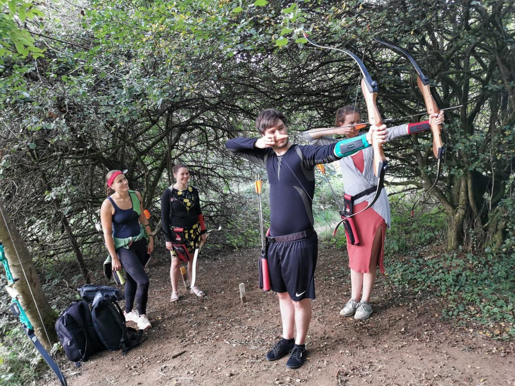 Eine Gruppe junger Leute bekommt von einer Trainerin die Grundlagen des Bogenschießens beigebracht.