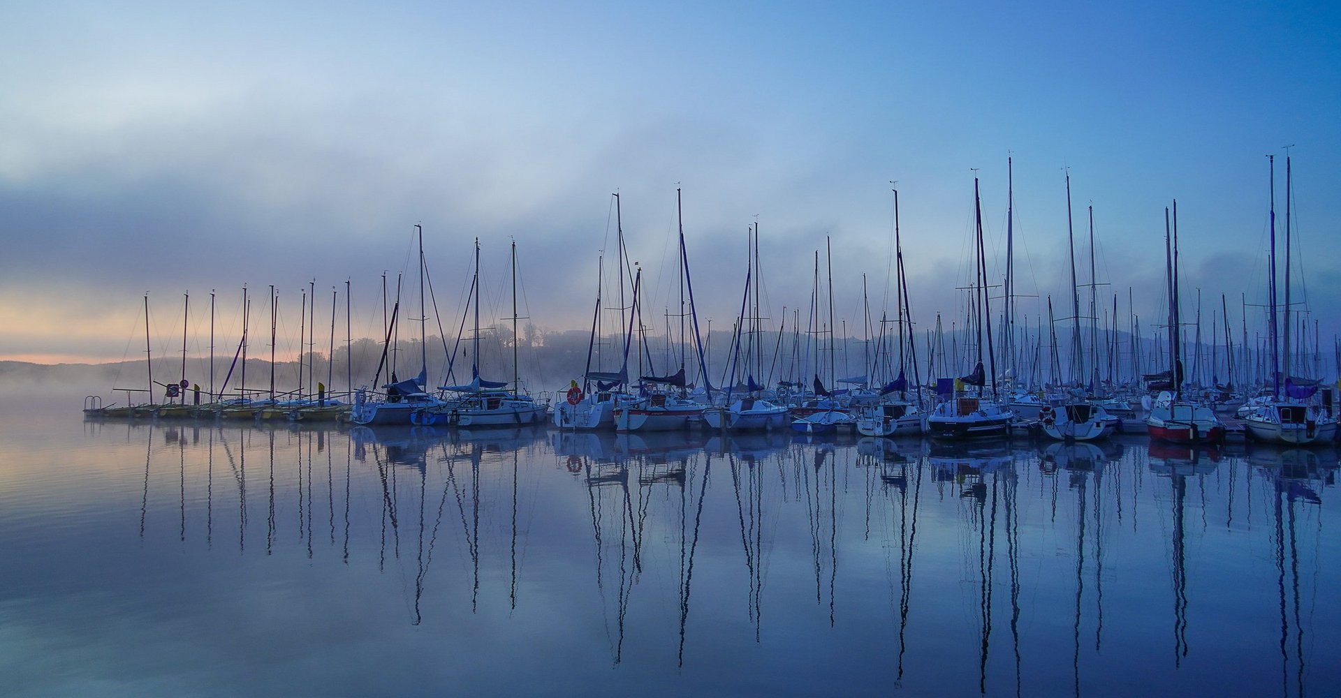 Der Segelhafen mit seinen verschiedenen Segelbooten ist in Nebel gehüllt.