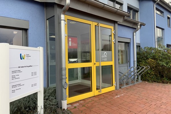 Die gelbe Eingangstür der Tourist-Information ist geschlossen. Daneben steht eine Tafel mit den Öffnungszeiten.