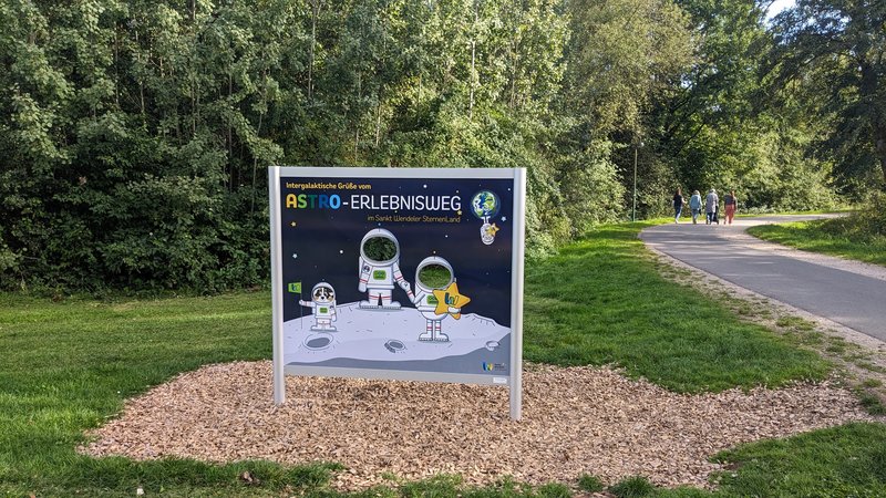 Die Gucklochtafel befindet sich auf dem Astro-Erlebnisweg am Seerundweg. Darauf sind die beiden Maskottchen Wenda (ein Schaf) und Linus (ein Hund) in Raumanzügen zu sehen - allerdings ohne Kopf. Dort, wo der Kopf sein sollte, kannst du selbst deinen Kopf hindurchstecken und ein Erinnerungsfoto schießen lassen.