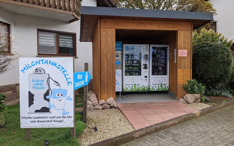 Ein kleines Holzhaus am Straßenrand, in dem man Milch und andere Produkte vom Bauer vor Ort erwerben kann.
