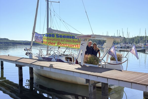 Ein Mann und eine Frau stehen auf einem Segelboot, das im Hafen liegt