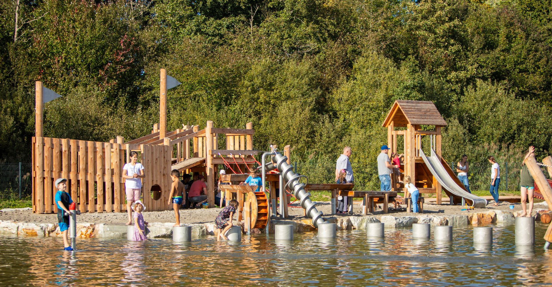 Eltern und Kinder verschiedener Altersstufen spielen an Klettergerüsten und im Wasser