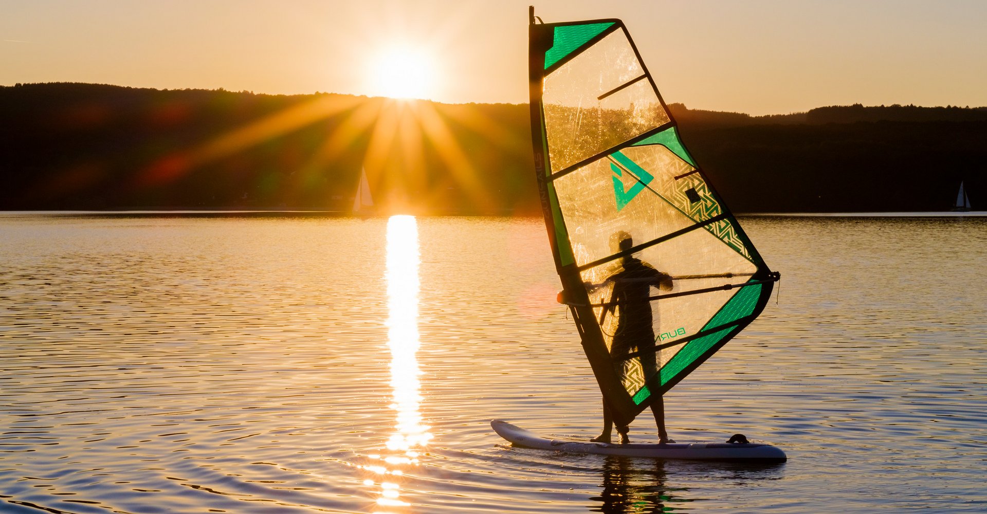 Ein Surfer auf dem Bostalsee, die Sonne geht im Hintergrund unter.