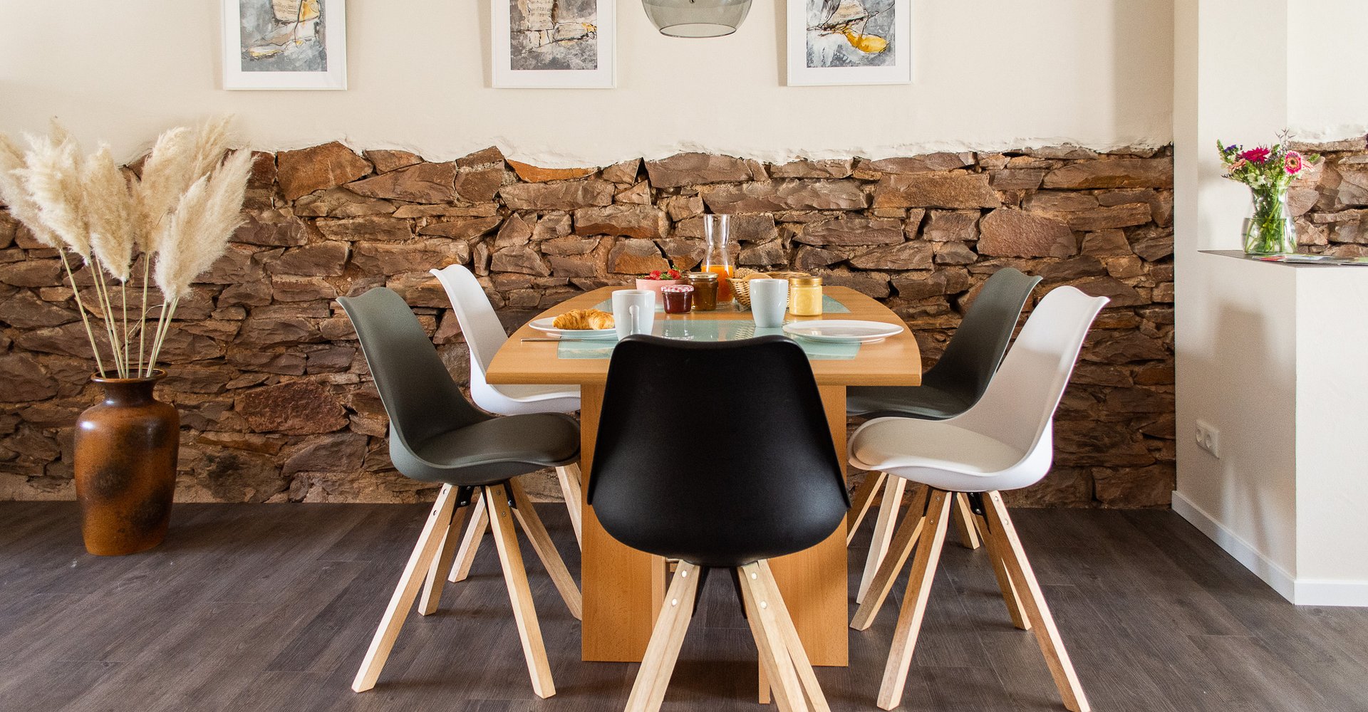 Ein Esszimmer mit Esstisch und Stühlen. Dahinter hängen Bilder an der Wand und etwas Dekoration steht im Raum.